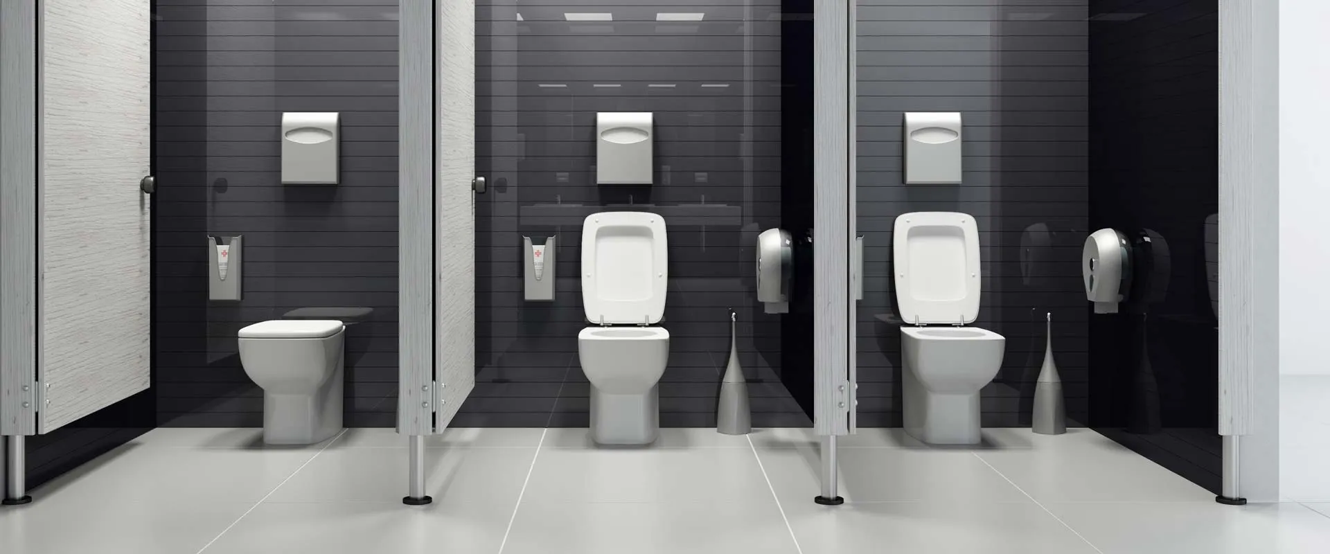 Baño de uso comercial con mamparas divisorias y sanitarios blancos sobre muro oscuro