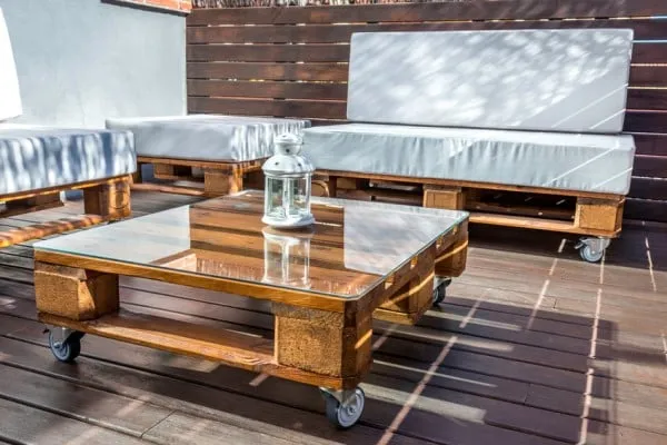 Sala de terraza en madera con mesa de centro de cristal y cojines claros