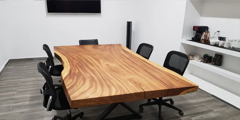 Sala de juntas con mesa de madera de canto natural, sillas de oficina y nicho para café