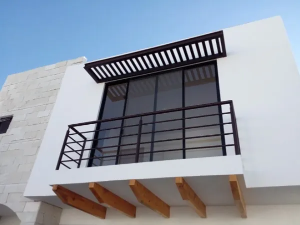Balcón con barandal de acero oscuro, celosía de sombra y vigas de madera bajo la losa