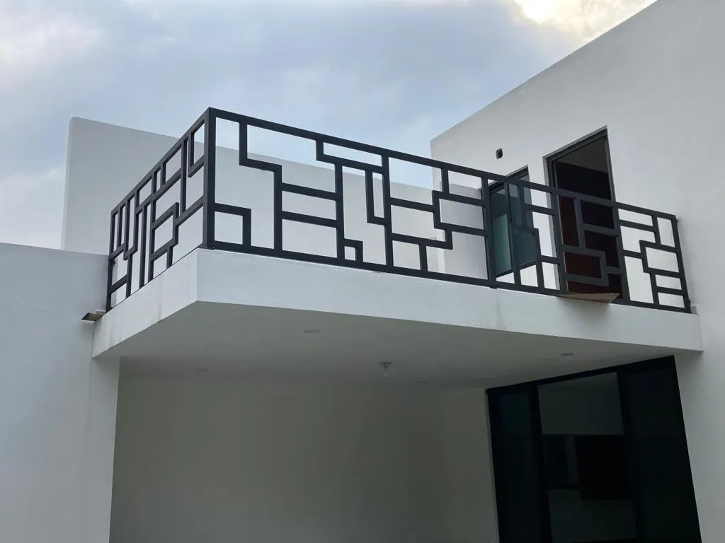 Barandal de acero negro con diseño geométrico en el balcón de una casa blanca
