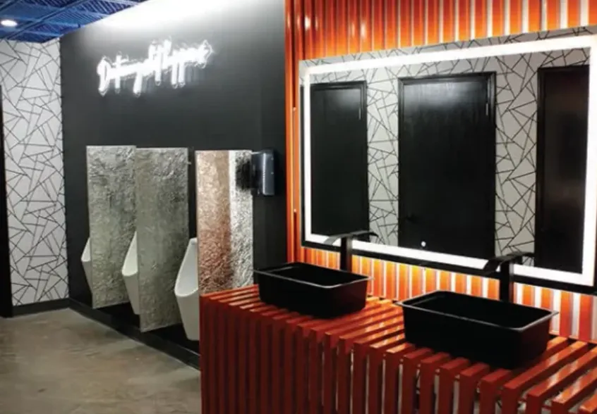 Baño de local comercial con cubierta de madera naranja, lavabos negros, espejos retroiluminados y letrero de neón